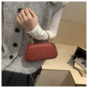 Close-up of red rhinestone evening clutch with gold bamboo-style handle and chain strap
