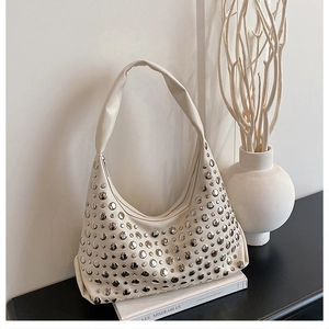 Detail of a creamy white hobo bag with silver rivets, shown in a minimalist setting