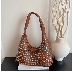 Detail of brown hobo bag with silver studs on leather surface placed on a book