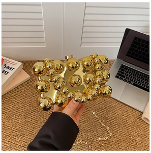 Detail einer goldenen Acryl-Clutch mit glänzenden Perlen und einer feinen Metallkette