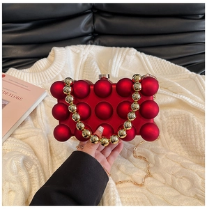 Detail einer roten Acryl-Clutch mit Kugelstruktur, Goldgriff und feiner Metallkette