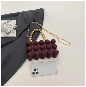Makro-Detail der weinroten Acryl-Handtasche mit Goldperlen-Griff und feiner Kette