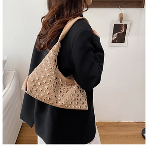 Close-up of beige shoulder bag with silver rivet details worn by model in black suit