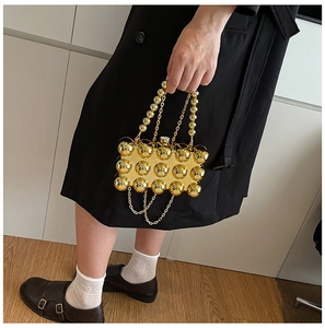 Detailaufnahme der goldenen Kugel-Clutch mit Perlengriff und hängenden Metallketten