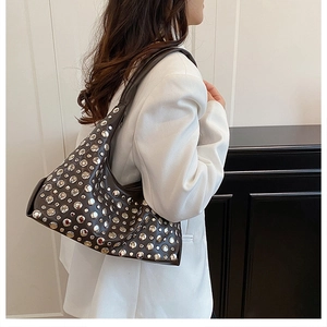 Model wearing dark leather underarm bucket bag with silver rivet studs on white blazer