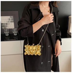 Detailaufnahme einer goldfarbenen Abendtasche mit Kugelverzierung und langer Metallkette