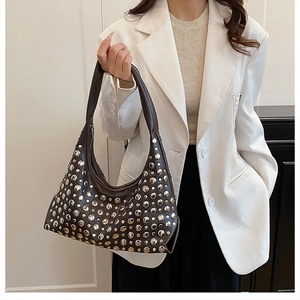 Detail of dark rivet studded crescent underarm bag styled with a beige blazer outfit
