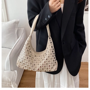 Detail of a chic cream crescent bag with silver studs held by a model in a black blazer