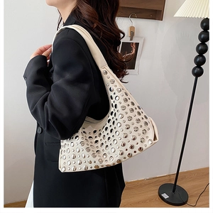 Detail of cream white moon-shaped hobo bag with silver rivets worn over a black suit