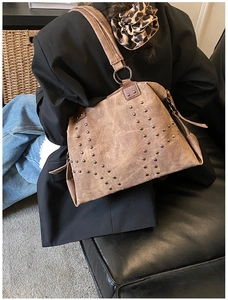 Detail of vintage brown tote bag featuring metallic rivets and wide shoulder strap