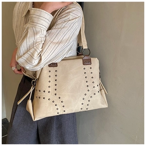 Detail of beige tote bag showing metal rivets, large ring hardware and reinforced brown trim