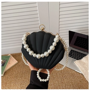 Close-up of black shell-shaped acrylic evening bag with faux pearl handle and gold clasp