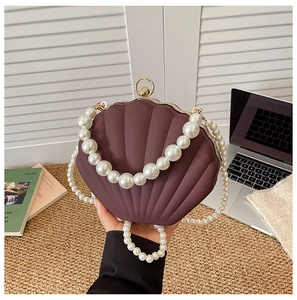 Detail view of shell-shaped acrylic handbag with pearl strap and golden hardware