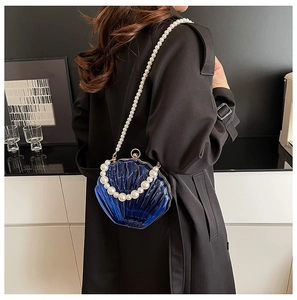 Macro view of a blue shell-shaped acrylic evening bag with large pearl strap and clasp