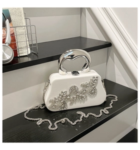 Detail of white evening box bag featuring sparkling rhinestone flowers and silver U-handle