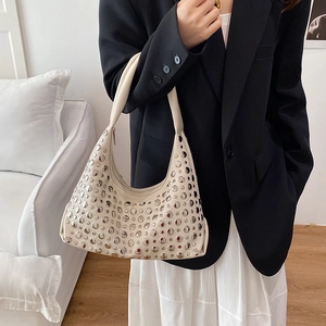 Vintage beige Hobo bag with silver studs worn by a model in a minimalist setting