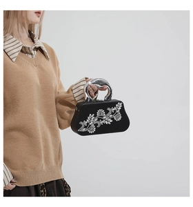 Close-up of black evening clutch bag with crystal flower motif and silver metal handle