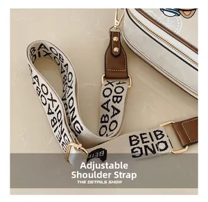 Detail of adjustable beige woven shoulder strap with letter pattern and gold metal hooks
