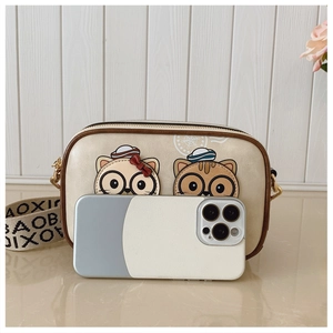 Detail showing cream camera bag with cute cat prints and a wide logo strap next to a phone