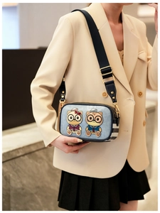 Detail of blue cartoon cat crossbody bag featuring wide fabric strap and gold hardware