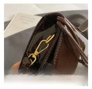 Detail shot of golden metal hook and stitching on dark brown patent leather handbag