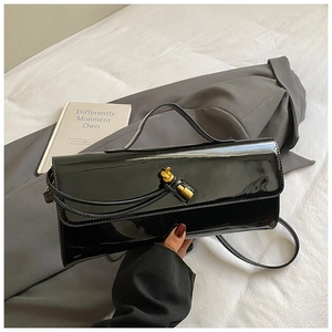 Detail of black patent leather crossbody bag with golden knot buckle on blazer