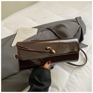 Detail of glossy brown leather shoulder bag with stylish knot buckle and gold metal accents
