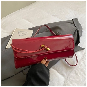 Detail of burgundy glossy patent leather handbag with a golden metallic twist-lock
