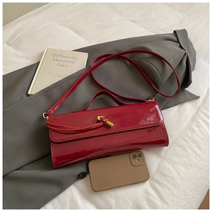 Detail of red patent leather handbag with gold knot buckle on grey suit background