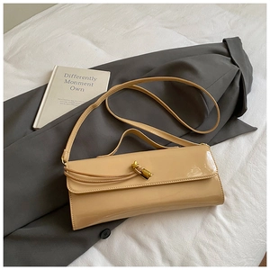 Detail of beige patent leather bag with gold buckle on grey blazer and art book