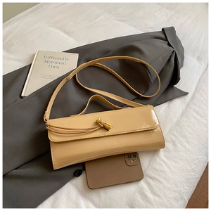 Chic beige glossy leather shoulder bag with gold twist clasp on a white textured backdrop