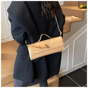 Detail view of a glossy beige patent leather crossbody bag with a gold knot buckle