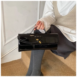 Close-up of a glossy black patent leather handbag with a knotted gold metal clasp