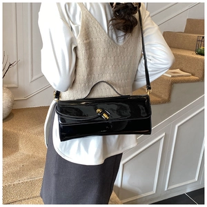 Close-up of a glossy black patent leather handbag featuring a golden twist-lock closure