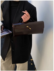 Detail of dark brown glossy patent leather bag with a golden metal twist buckle
