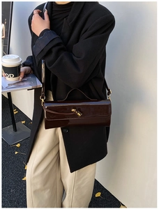 Detail of dark brown patent leather shoulder bag with gold twist lock on autumn street background