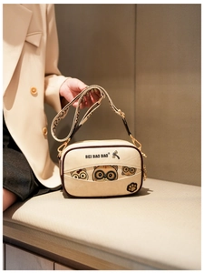 Detail of beige cartoon crossbody bag featuring cat illustration and wide fabric strap