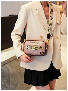 Detail of pink cartoon cat box bag featuring wide embroidered strap and gold metal hardware