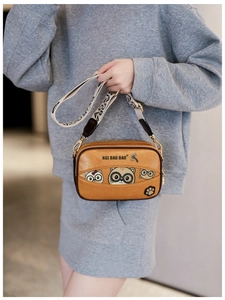 Close-up of a camel cartoon cat crossbody bag with a wide patterned strap on a model