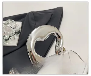 Detail of transparent acrylic barrel bag featuring a sleek silver metal handle and chain