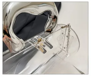 Close-up of clear acrylic cylinder bag with bold silver metal handle and gold buckle