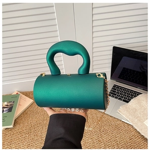 Detailed close-up of dark green cylindrical bag with round handle and gold chain strap