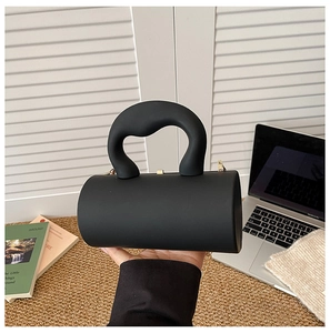 Detail of black acrylic cylinder bag with smooth matte finish and gold chain strap