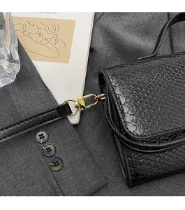 Close-up of black snake texture handbag featuring shiny gold hardware hooks and strap