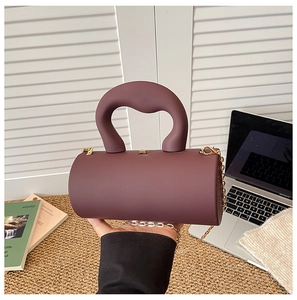 Macro detail of wine red cylindrical bag with chunky handle and golden chain strap