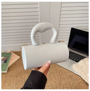 Detail of matte white cylindrical handbag with thick handle and gold chain strap