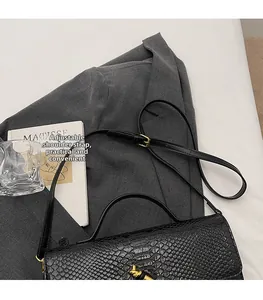 Close-up of black crocodile pattern shoulder bag with adjustable strap and gold lock