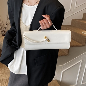 Glossy white rectangle shoulder bag with gold twist buckle in elegant indoor setting