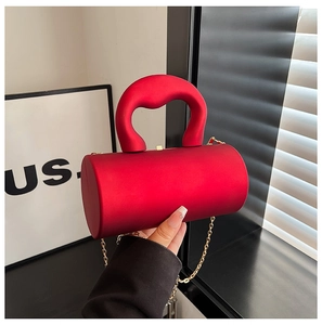 Close-up of red cylindrical acrylic handbag featuring thick handle and gold chain strap