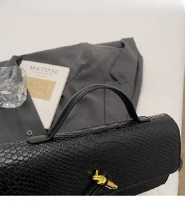 Detail of elegant black snake pattern handbag with gold knot metal clasp and smooth handle